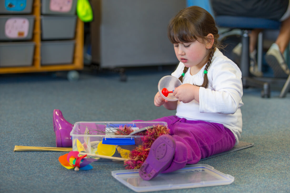 A child sit exploring a container of toys