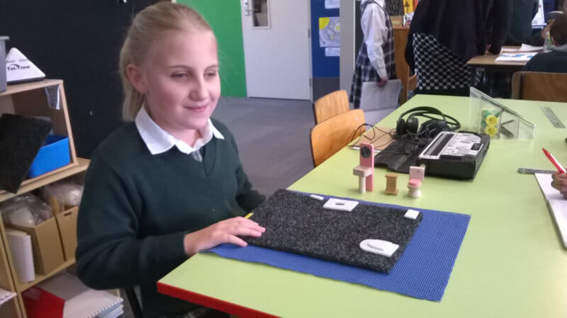 Young student sitting at table with map and 2D shapes, building a map