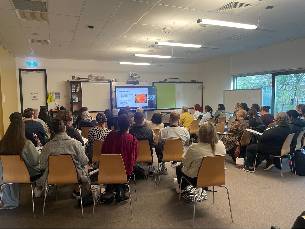 A room filled with adults watching a large screen