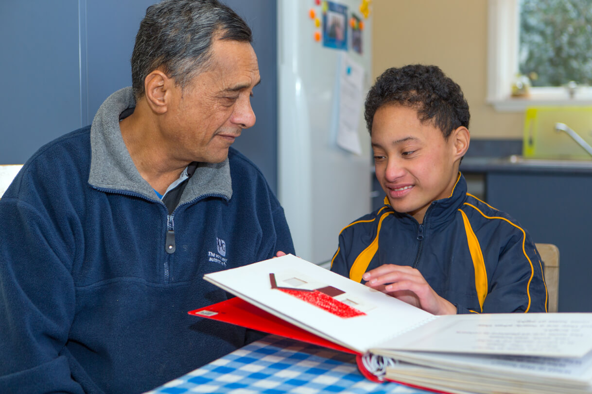 Boston sitting in front of a braille book at the kitchen table with his dad.