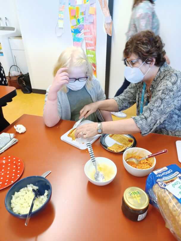 Child and lady sitting at a table cutting up food.