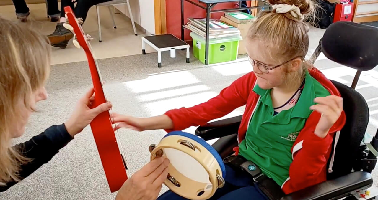 Child choosing between a ukulele or tambourine which the teacher is holding