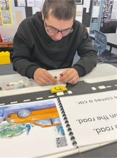 A child is re-enacting the picture from the Stop PM reader on the Wise Walker by using the Lego people to check both ways before they cross the road.