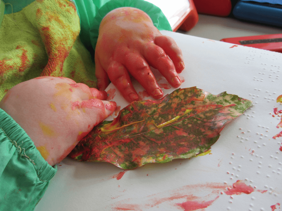 Child’s hands using fingerpaint on a large leaf.