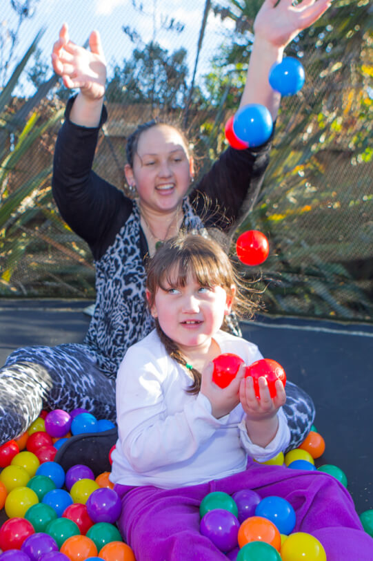 Giana and her mum sit on the trampoline with coloured plastic balls.