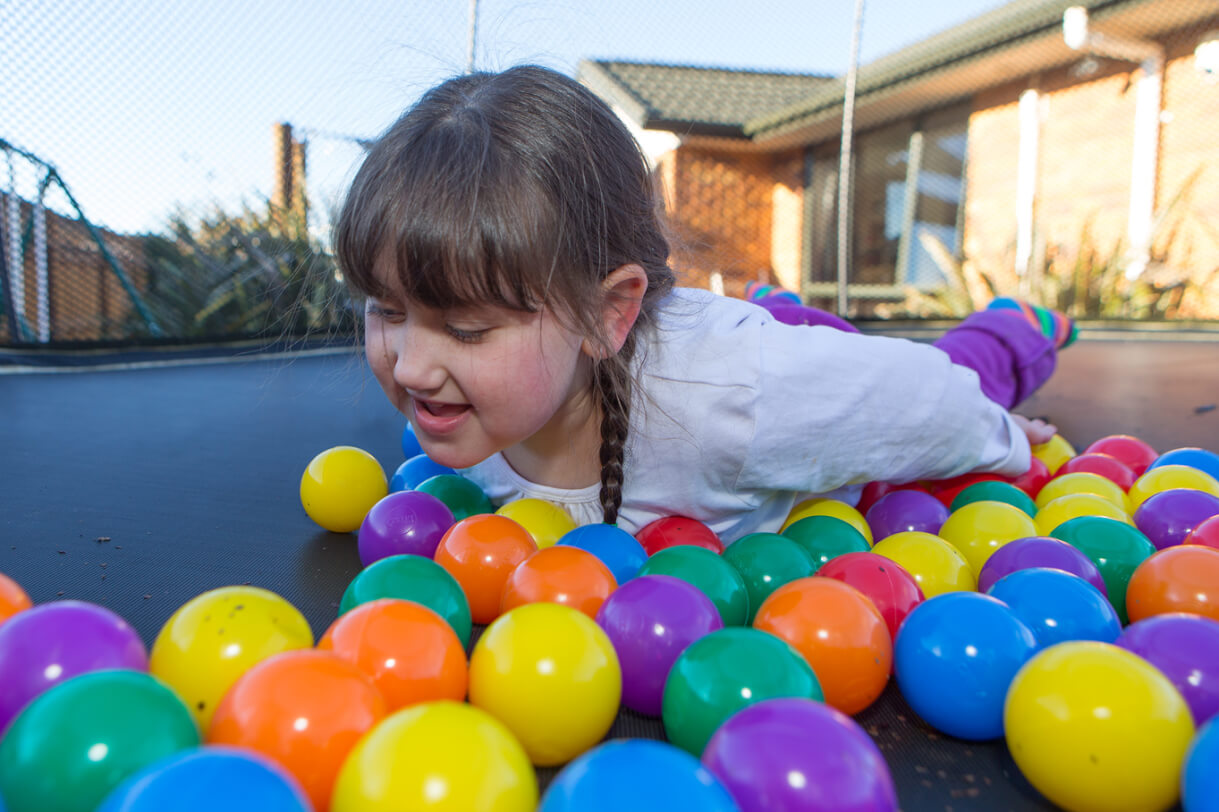 Giana lying on the trampoline surrounded by coloured play balls.