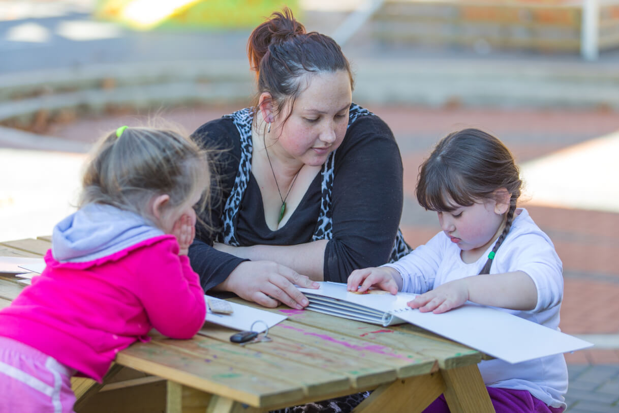 Giana sitting outside at a table with her mum and sister.