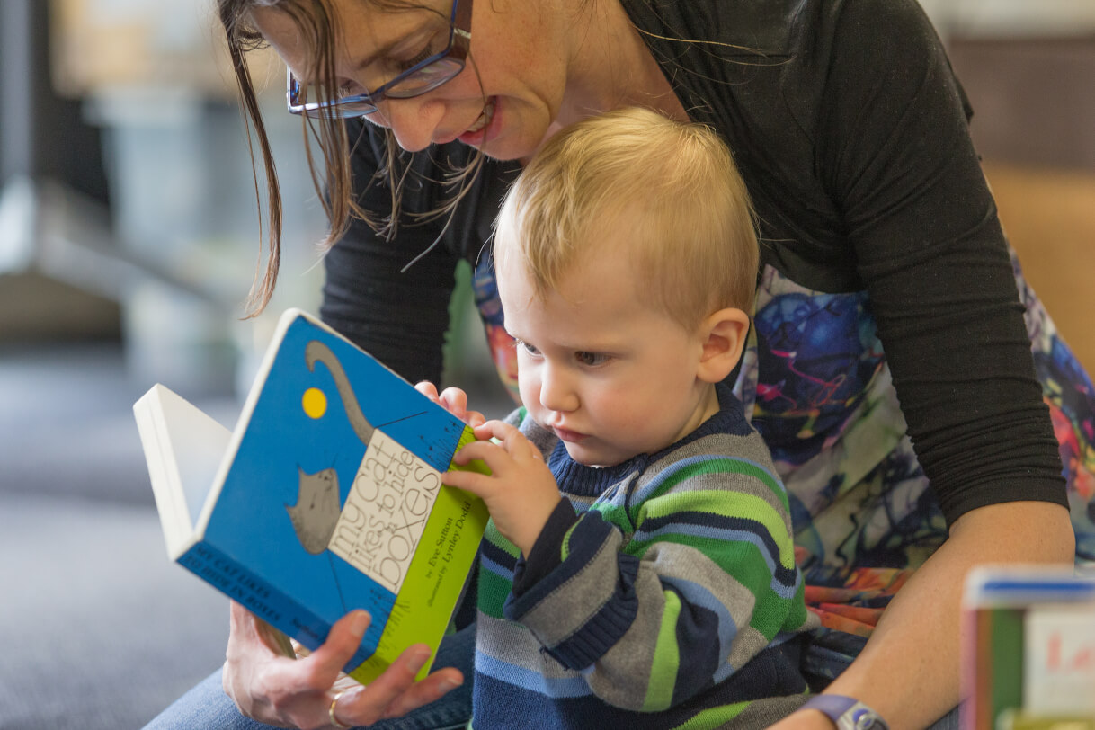 Child sitting and reading a book with his mum