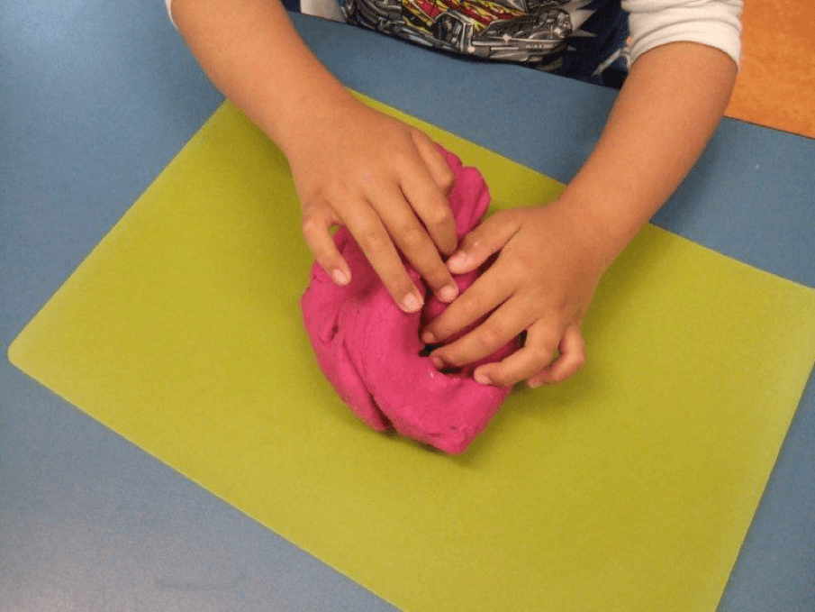 Child’s hands exploring a lump of pink playdough.