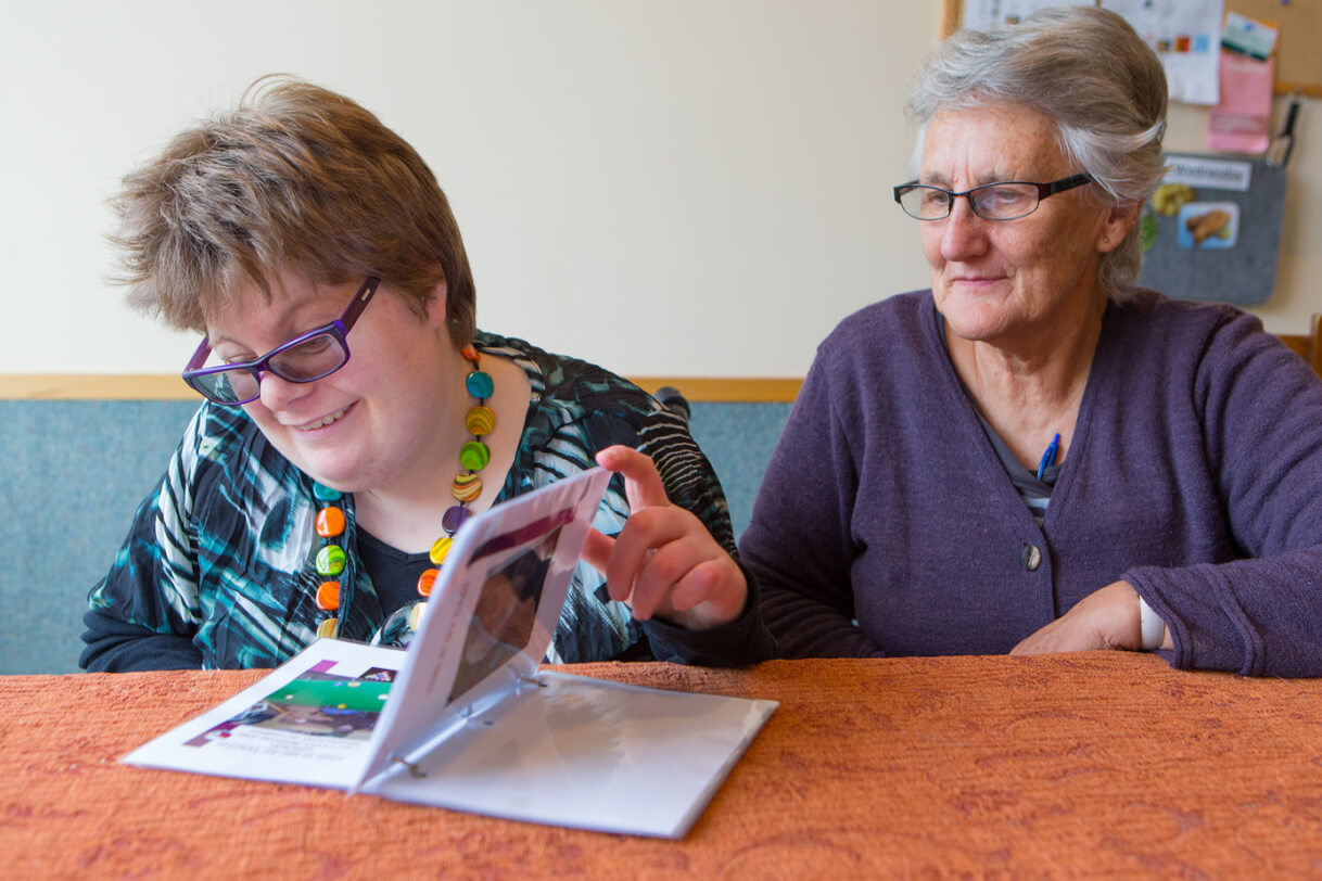 Katelyn sitting at a table with her carer reading a book.