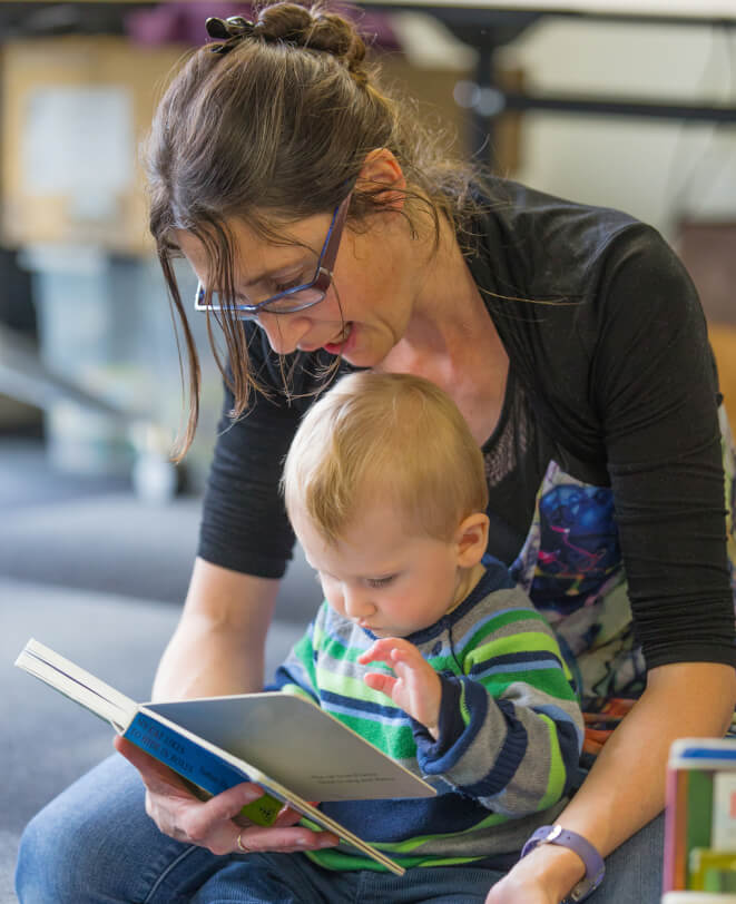 Robert sitting on mum's knee looking at a book.