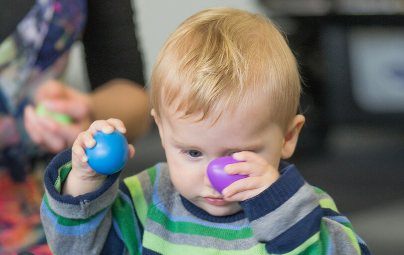 Robert sitting holding small coloured balls looking at purple.