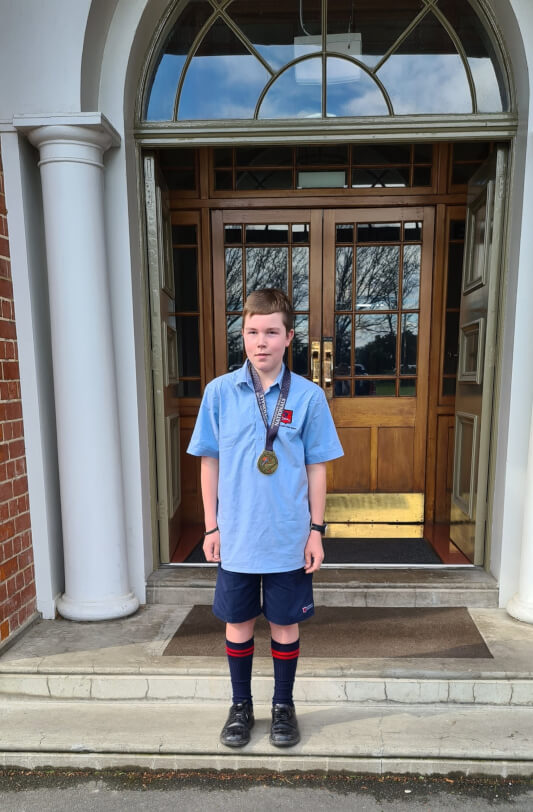 Student standing outside a building with his medal around his neck.