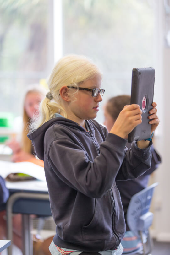 Olivia standing taking a photo on an iPad.