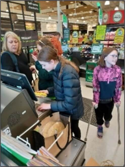 Zaria using the self-checkout machine at the supermarket to purchase grocery items with Jayne's support.